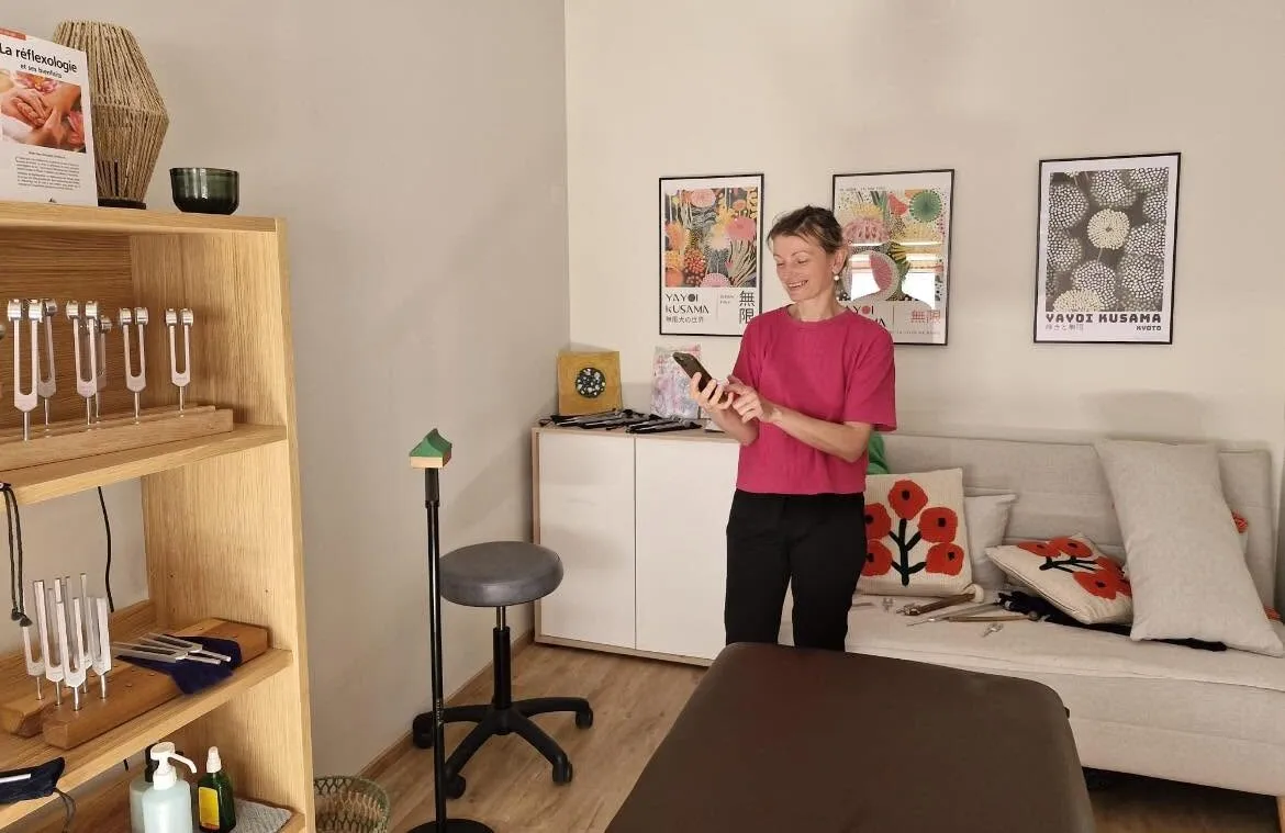 Krystyna Butryn dans son cabinet de Perpignan, devant l'étagère de diapasons thérapeutiques, avec la table de soin et le coin salon