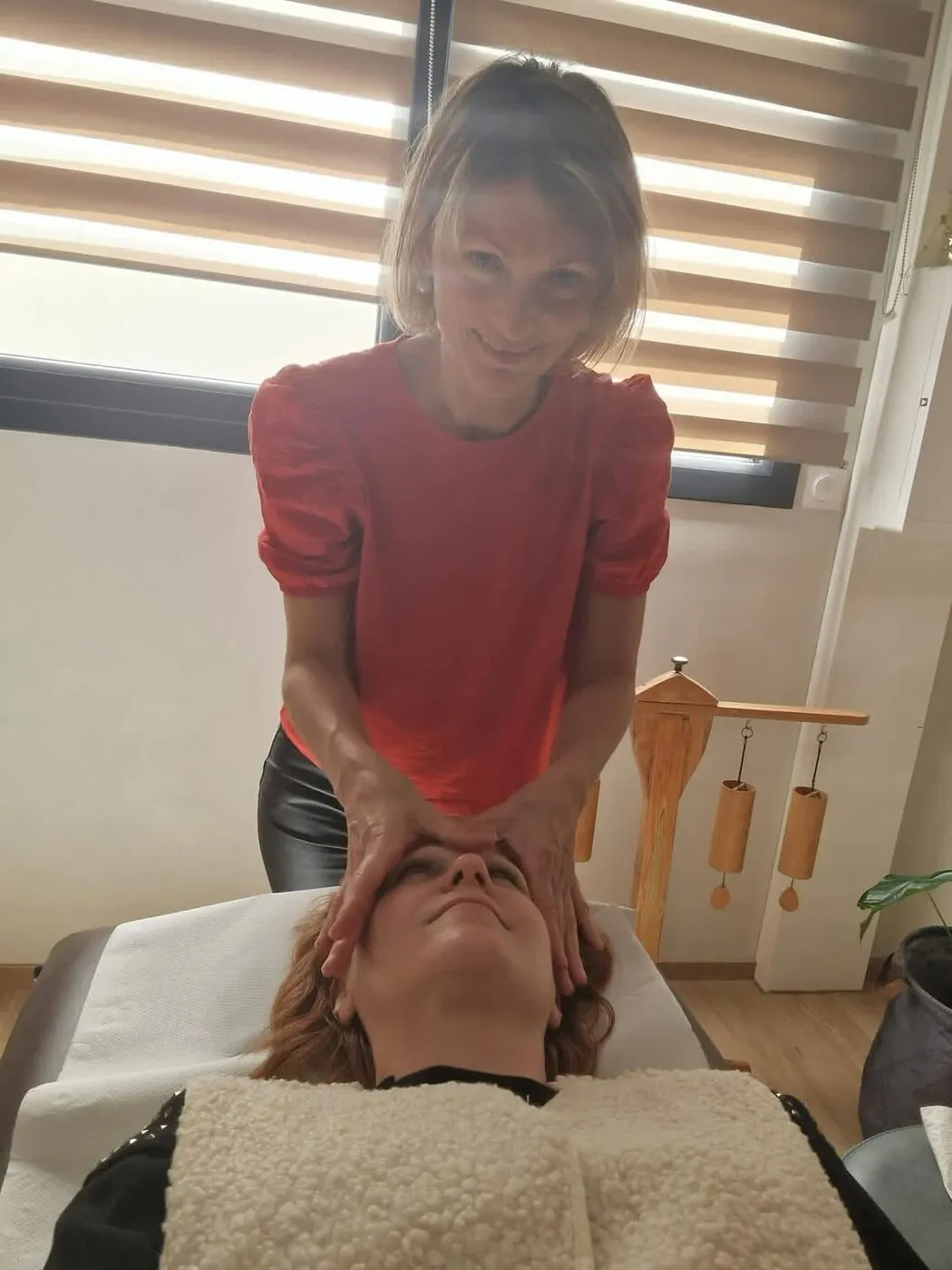 Krystyna Butryn, debout au-dessus de la table de soin, pose ses mains sur le front d'une personne allongée pendant une séance au cabinet